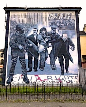 Bloody Sunday (1972) memorialized in mural by Payton Walton, 2018, showing hero-priest Fr. Edward Daly in Belfast and men carrying body of young victim. 